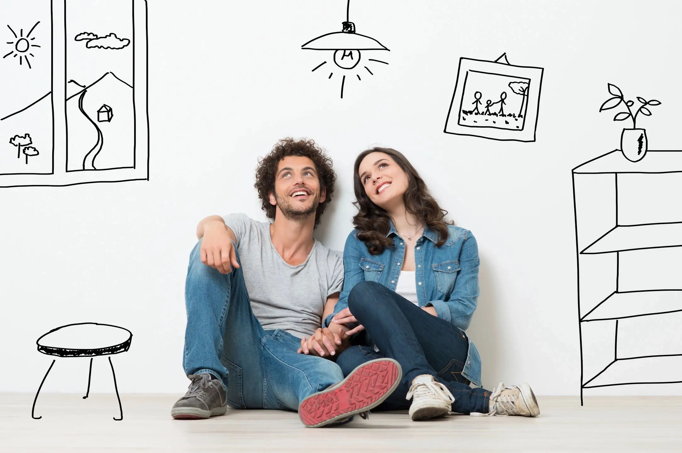 Couple in casual clothes sitting and relaxing against a white wall with playful doodles.
