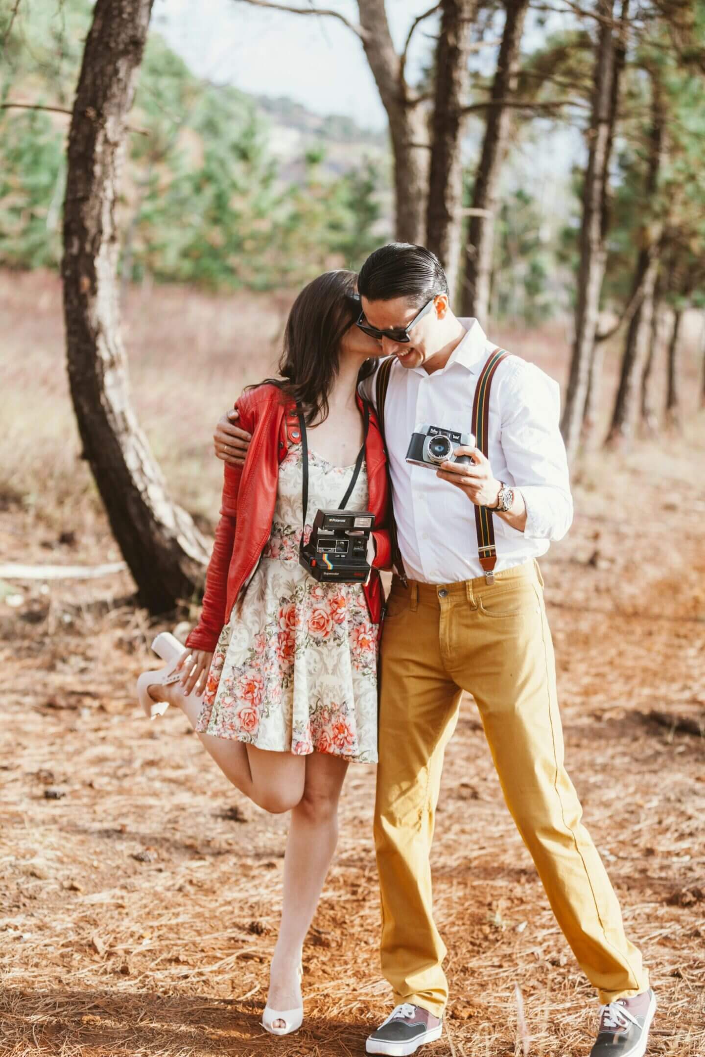 Couple sharing a tender moment in a forest with cameras around their necks.