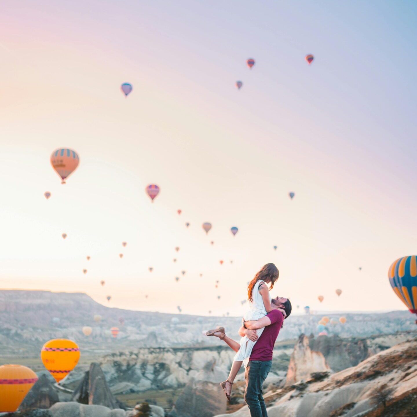 Woman tossing a child in the air with hot air balloons in the background.